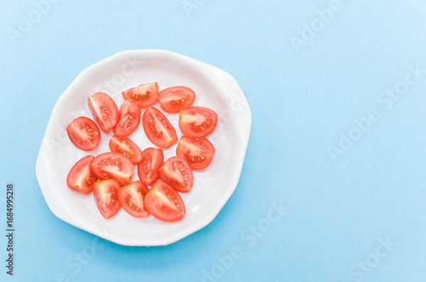 Fototapeta terrina in porcellana bianca com pomodorini freschi tagliati a spicchi su uno sfondo azzurro chiaro