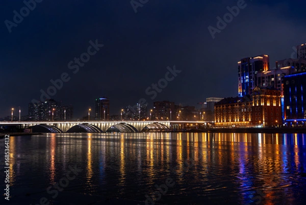Fototapeta Panoramic view of the river in central Yekaterinburg with Bazhovsky Bridge in the distance. Cloudy sky and autumn or spring season create a moody atmosphere.