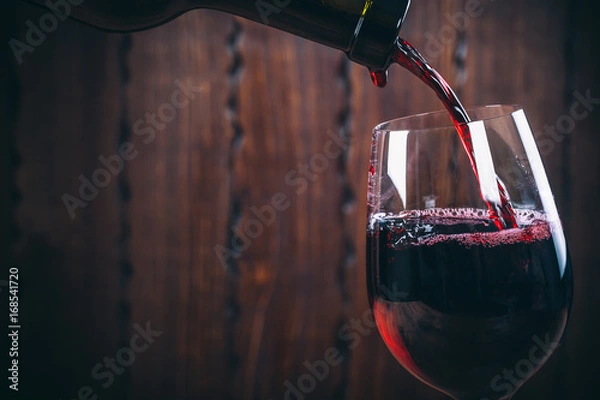 Obraz Pouring red wine into the glass against wooden background