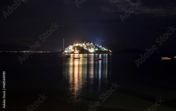 Fototapeta Illuminated daskaleio rocky island with church of the twelve apostles at night in tolo bay greece with reflections on calm sea