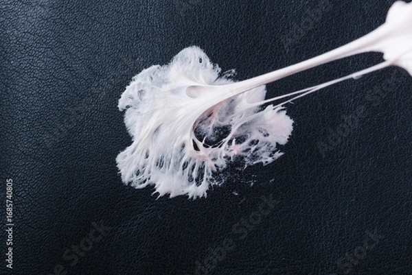 Fototapeta Chewing gum has become stuck on a black leather textured surface, showing its stretching and gooey consistency. Concept of daily stains. Spot-cleaning sticky mess upholstery seating. top view. 