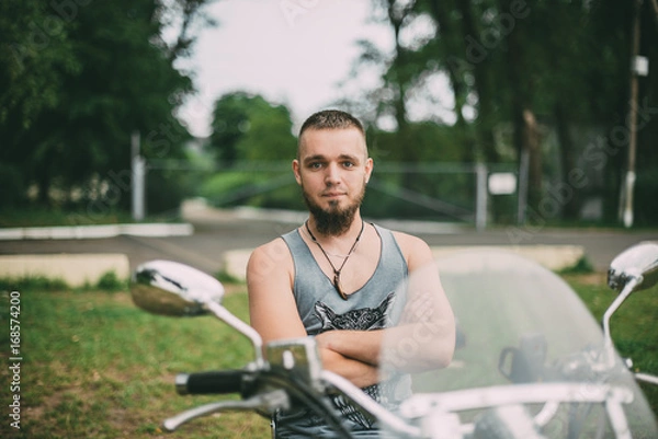 Obraz Красивый молодой мужчина с бородой сидит на мотоцикле на фоне природы