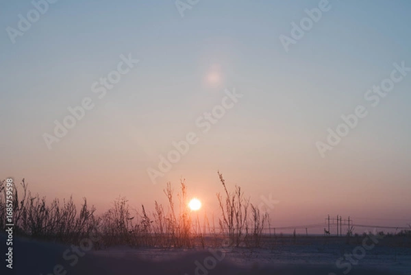 Fototapeta Frosty winter sunset in the field. Beautiful sunset in the snowy desert. Ice and sun..