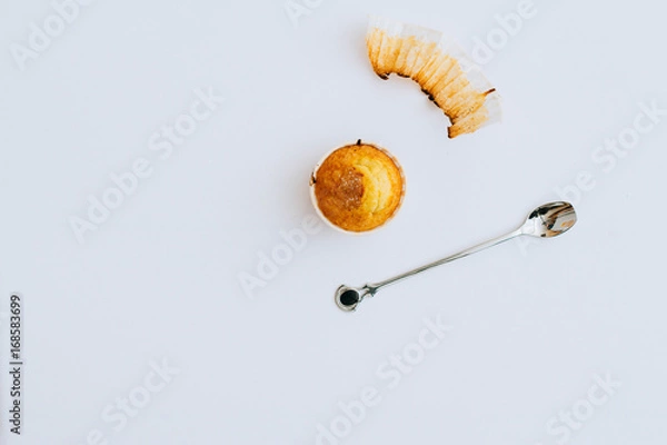 Fototapeta One orange cupcake on a white background, a cake wrapper, a metal spoon, minimalism