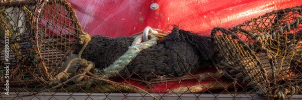 Fototapeta Panorama of crab pots on quayside with hull of small red boat in the background
