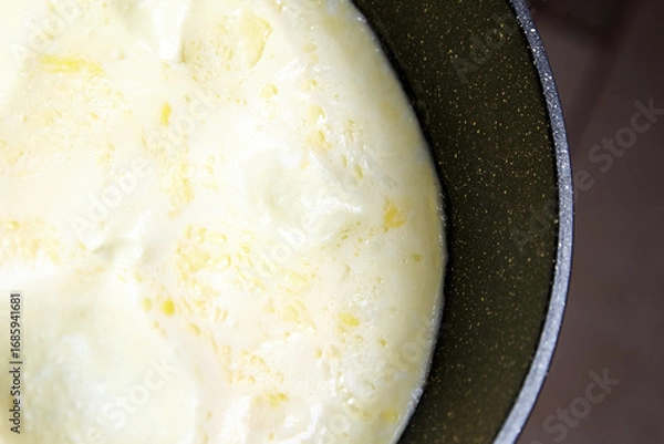Fototapeta Whisked eggs in a frying pan, bubbling gently on a stovetop, showcasing the cooking process of a delicious omelette, with a focus on texture and color variations