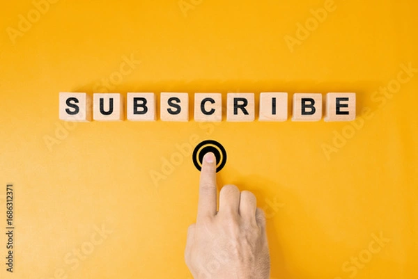 Fototapeta Male hand pressing subscription button with the word subscribe written on wooden blocks. Concept of online registration.