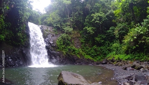 Fototapeta Lush waterfall cascading into a tranquil pool amidst dense tropical foliage