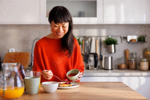 Fototapeta Woman adding berries to waffles while having breakfast at home