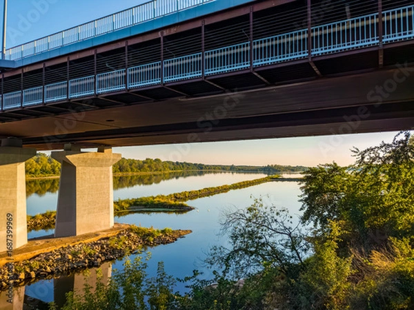 Obraz Under the bridge shot highlights its steel structure and concrete pillars, with the Vistula river and distant shoreline visible.