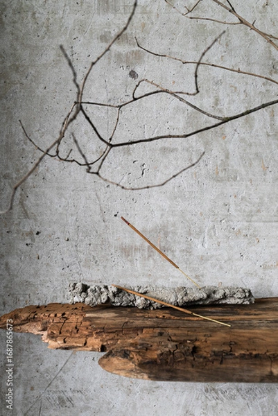 Fototapeta Minimalist still life in wabi-sabi style. Burning incense stick on a rustic holder, placed against a textured concrete wall.