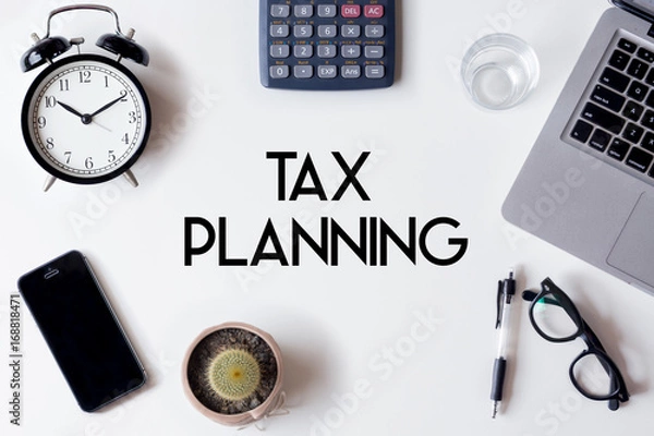 Fototapeta Tax Planning words written on white table with clock, smartphone, calculator, pen, cactus, glass and laptop