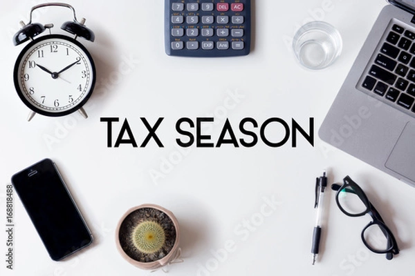 Fototapeta Tax Season words written on white table with clock, smartphone, calculator, pen, cactus, glass and laptop