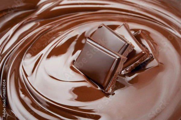 Fototapeta Melted pieces of chocolate bar in glossy chocolate splash background. Front view.