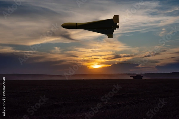 Fototapeta A military drone flies over a field in the rays of the setting sun.