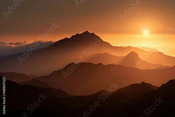 Fototapeta Golden sunset over a mountain range. Silhouettes of peaks bathed in warm light
