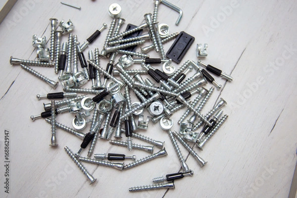 Fototapeta Furniture fasteners are poured out in a heap on furniture parts. Preparation for the assembly of cabinet furniture, unpacking and laying out fasteners and furniture parts