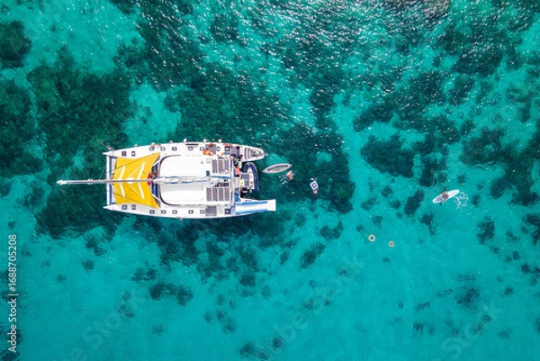 Fototapeta Aerial top view of sailing catamaran anchor over turquoise water with tourists swimming and paddle boarding at Racha Yai Island, A popular destination for summer vacation in Phuket, Thailand.