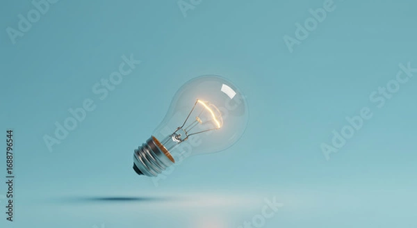 Obraz Glowing incandescent lightbulb levitates against a pale blue backdrop.