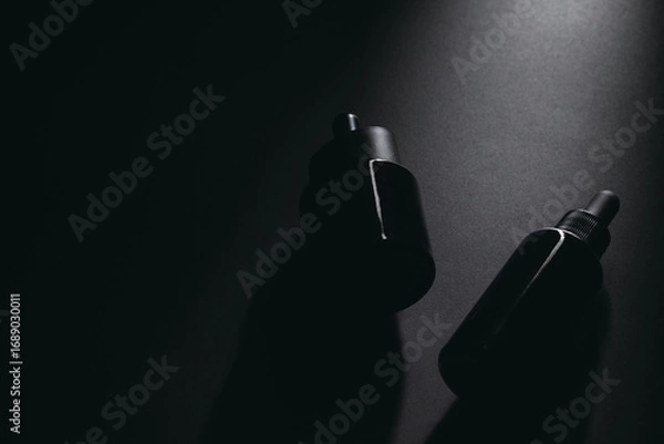 Fototapeta Minimalist dark dropper bottles on black background with dramatic lighting