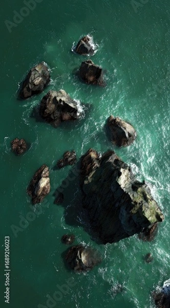 Obraz Overhead view of dark rocks surrounded by turquoise sea water. Waves crash gently against the stones, creating a serene, isolated scene