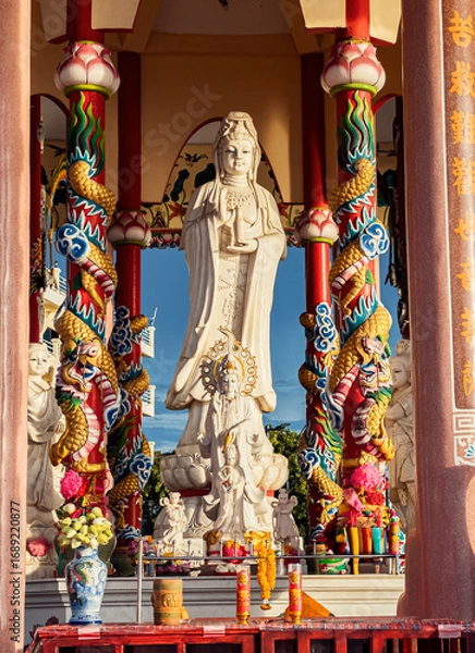 Fototapeta Large statue of Guanyin in colorful temple with dragon columns during sunny afternoon. Sriracha, Thailand.