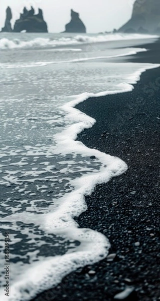 Fototapeta Foamy waves on a dark volcanic beach, basalt columns in the distance