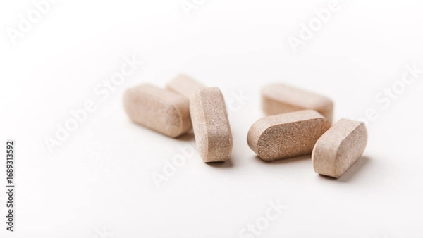 Fototapeta Lion’s mane mushrooms tablets that have beneficial effects on the body, especially the brain, heart, and intestines. Bright paper background. Soft focus. Close up. Copy space.	