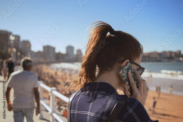 Obraz Young girl talking with her smatphone on the promenade