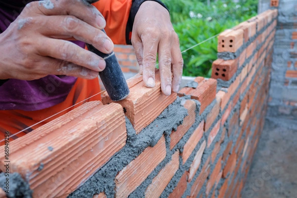 Fototapeta The hands of the construction workers are building a brick red brick wall