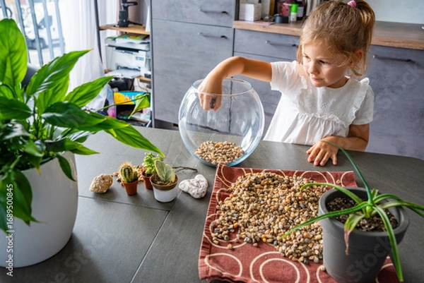 Fototapeta Little girl pouring stones into glass container to create drainage for future florarium or closed ecosystem. Hands-on learning, eco-friendly creativity and early involvement in nature-based projects.