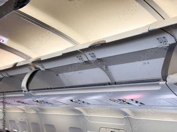 Fototapeta Overhead luggage compartments and cabin ceiling inside a passenger airplane. Travel, aviation, and the practical design of space in modern aircraft cabins.