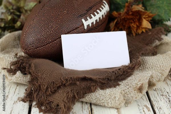 Fototapeta Blank white horizontal card mockup on fabric backing with rugby ball and dried maple leaves, soft natural light.