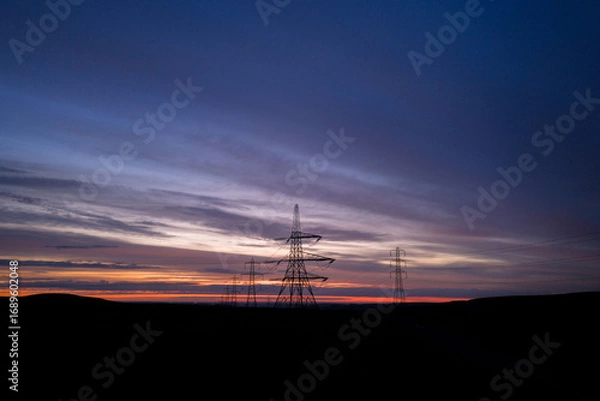 Fototapeta Electricity Pylons at Dawn Amid Vibrant Horizon in Rural Landscape