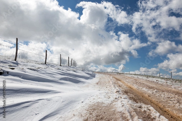 Fototapeta A mountain road with snow at the side, under a deep, blue sky with white clouds