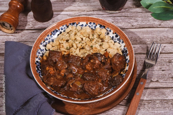 Fototapeta Delicious hungarian goulash with spaetzle, mushrooms and spices on rustic wooden table
