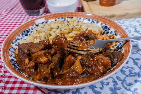 Fototapeta Fork lifting a piece of beef stew with spaetzle on the side, a hearty and flavorful meal