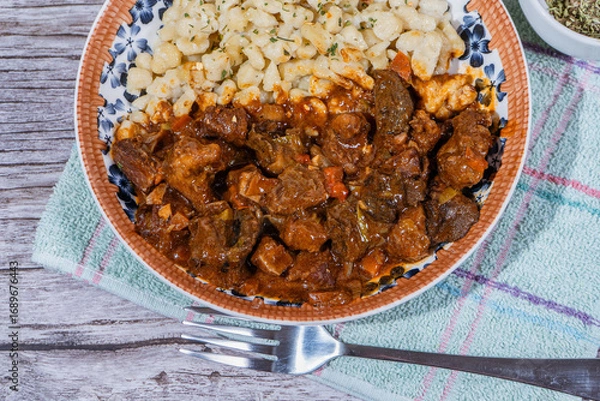 Fototapeta Delicious hungarian goulash with spaetzle on rustic wooden table
