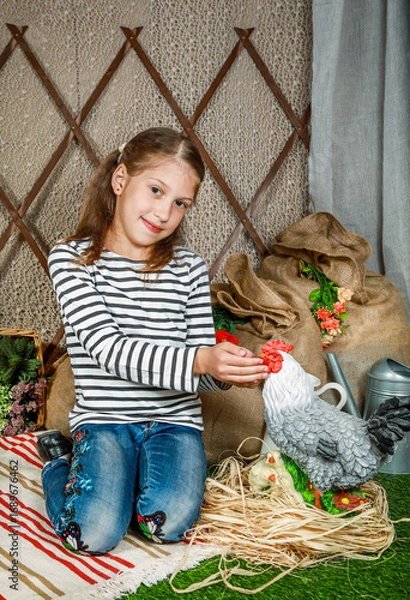 Fototapeta Girl playing with toy chicken in barn, surrounded by hay bales and farming tools