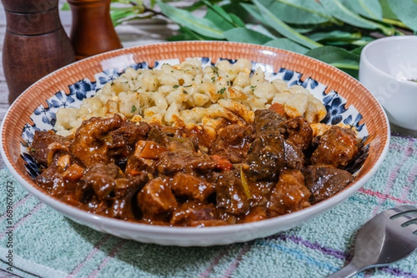 Fototapeta Delicious hungarian goulash with spaetzle, a traditional stew, resting on rustic table