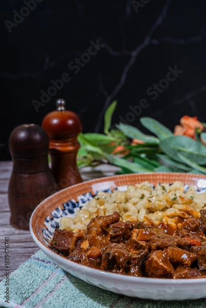 Fototapeta Delicious hungarian goulash with spaetzle on rustic table setting