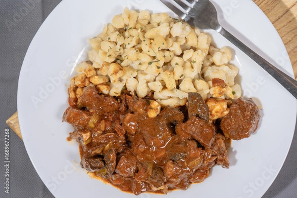 Fototapeta Delicious hungarian goulash with spaetzle garnished with parsley on white plate