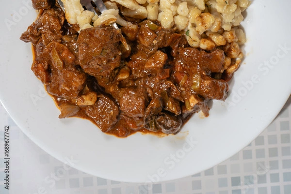 Fototapeta Fork lifting spaetzle from plate of beef goulash stew