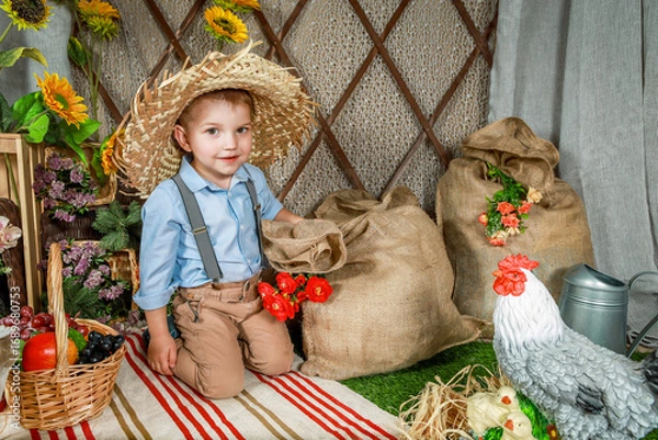 Fototapeta Adorable Little Farmer Boy Kneeling Next to Burlap Sack in Rustic Setting