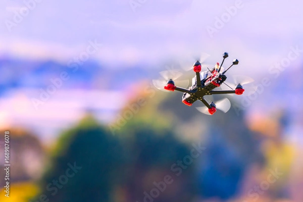 Fototapeta Fpv drone flying at high speed on a sunny day. The quadcopter is in the air viewed from the ground. 