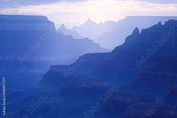 Fototapeta Misty purple and blue layered canyon landscape at sunrise with hazy distant cliffs and soft glowing light