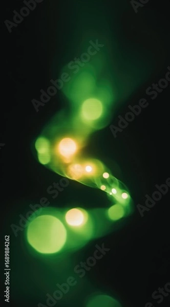 Obraz A blurred image of a flowing, green and gold light trail on a dark background creates a surreal, ethereal, and dreamy visual effect