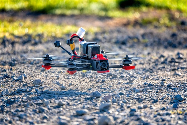 Fototapeta Fpv drone hovering above gravel on a sunny day. The quadcopter is flying a few centimetres from the ground