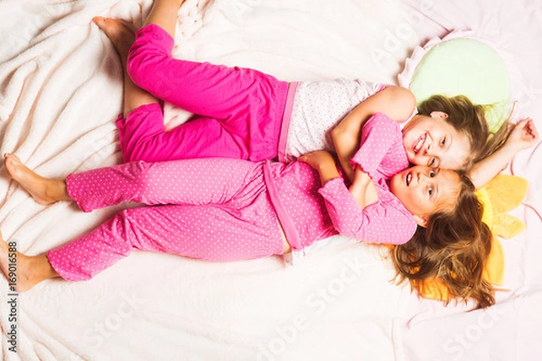Fototapeta Children with smiling faces lie on pink background and hug