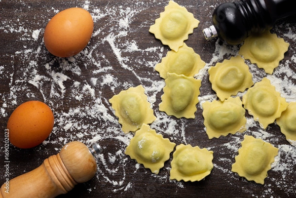 Fototapeta Fresh stuffed ravioli big size on wooden table with flour and eggs